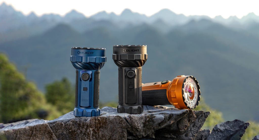 Olight Marauder 3 flashlights in Black, Midnight Blue, and Orange outdoors